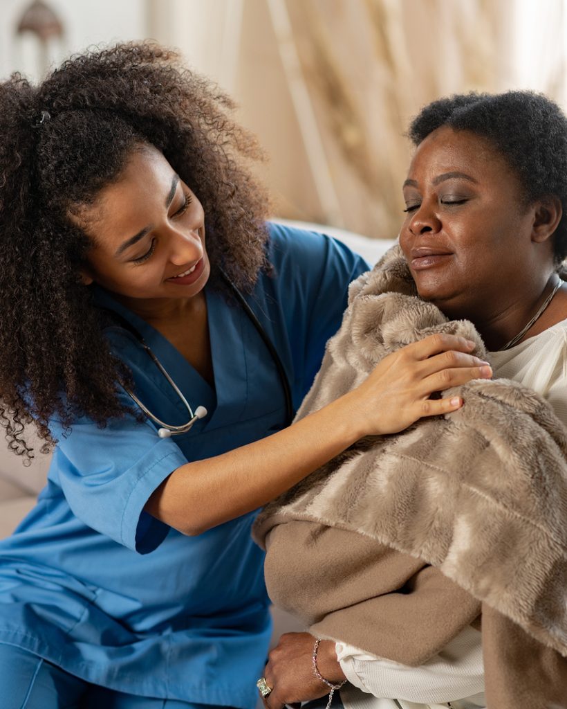 Caring curly nurse giving warm plaid to patient after catching cold