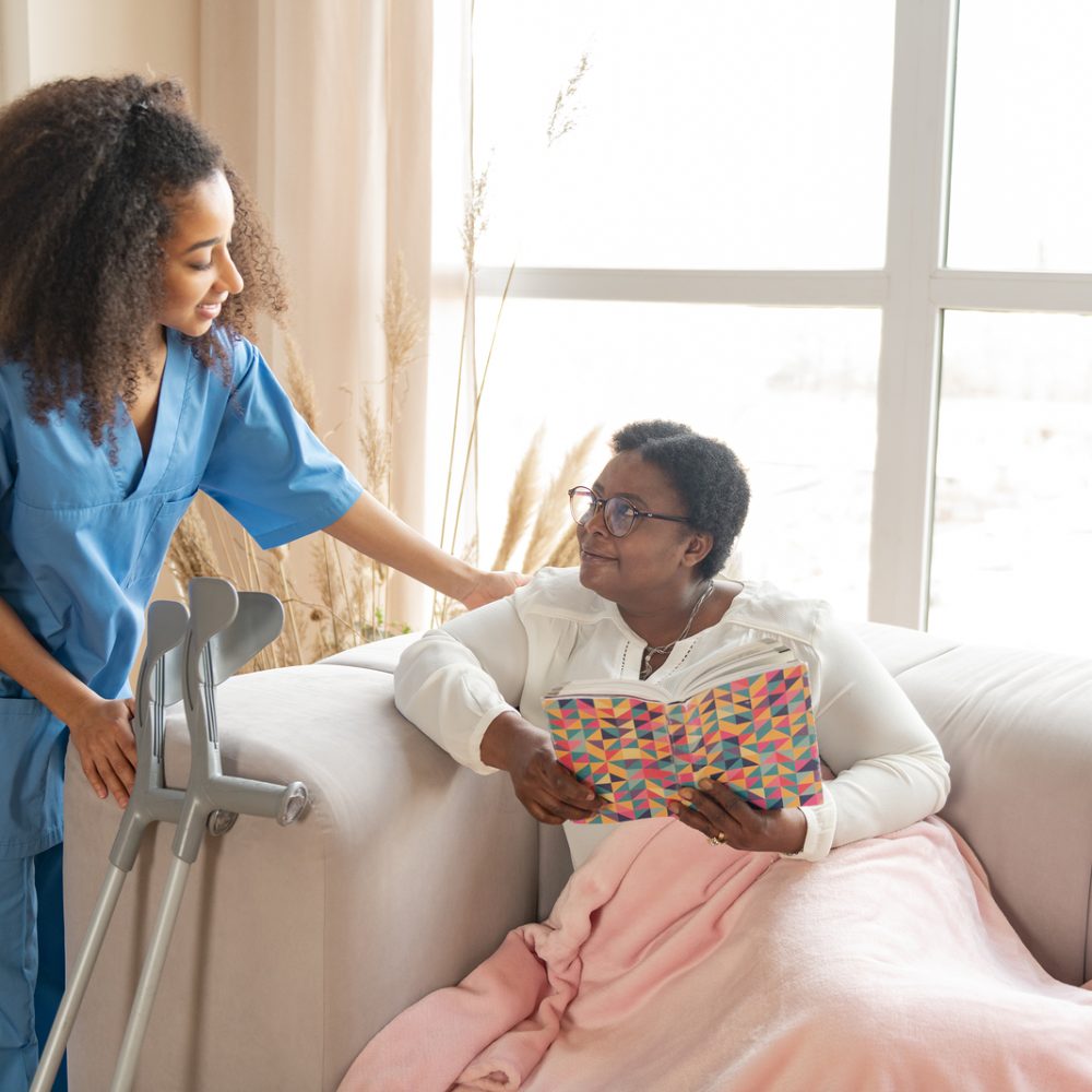 Woman with leg injury lying on sofa and talking to pleasant nurse